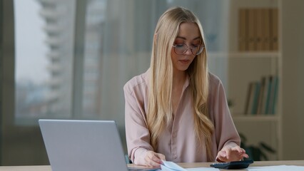 Caucasian business woman talking video call with laptop checking papers calculate company finance budget with document focused businesswoman female girl worker boss leader remote communicate in office