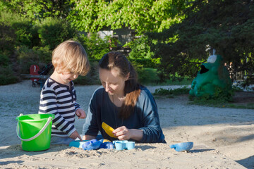 Mother and cute little child boy having fun playing with sand and colorful toys in the park, beautiful summer sunny day in children playground. Selective focus