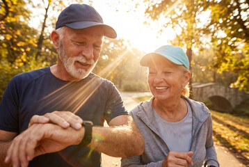 Active senior couple jogging in park tracking fitness on smartwatch with motion blur.