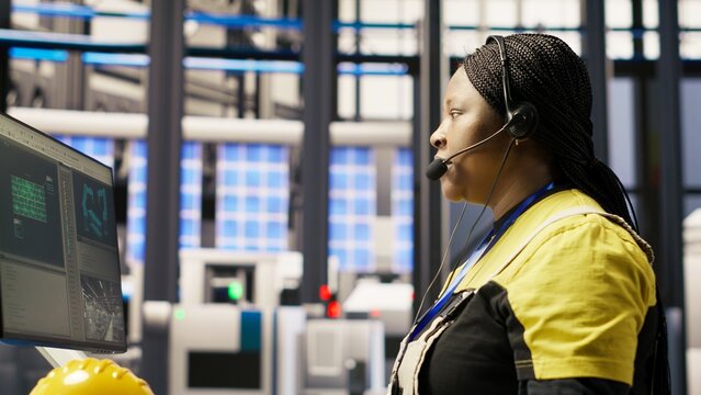 Call center agent in smart factory using headset to assist remotely with maintenance queries, monitoring automated solar panel assembly processes, providing technical guidance, camera B