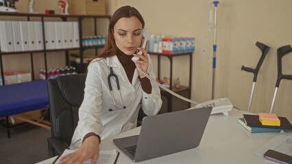Woman doctor with stethoscope holds phone and clipboard while reaching for papers in clinic building; calm care.