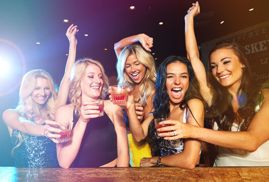 Excited, laughing and girl friends with cocktails at pub for disco, celebration or fun at event together. Bonding, smile and group of women at party with alcohol drinks at night club with energy.