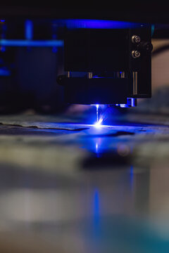Industrial laser cutting of paronite gasket material. CNC machine cutting sheet material with a blue beam. High precision manufacturing process of sealing parts for engineering and engines.