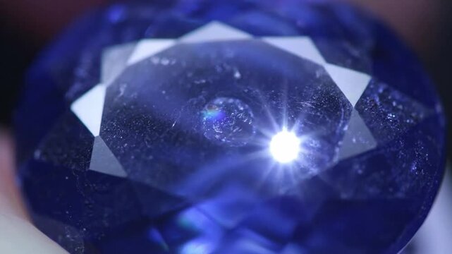 Close up macro shot of a faceted blue gemstone with internal inclusions and light reflections.