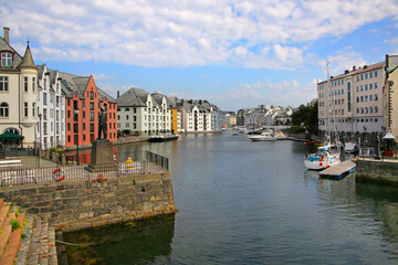 Colourful Art Nouveau historic buildings and boats along the  waterfront of the harbour or canal, Alesund, Norway. Statue in the foreground on the pier.