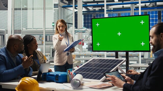 Businesspeople in photovoltaics plant look at data on mockup display. Solar panels factory management team and investor displaying deal terms on green screen monitor, camera A