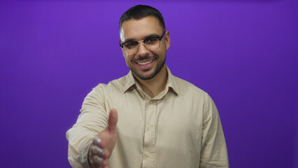 Man smiles and extends hand for a warm handshake in studio with vivid purple hue; greeting friendliness.
