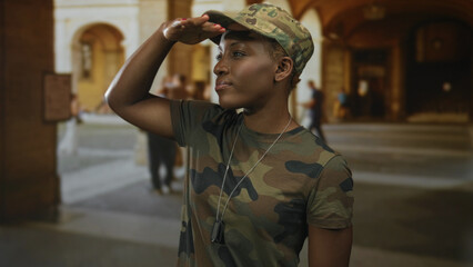 Young african american woman in camouflage uniform salutes with hand to forehead in street; pride service duty.