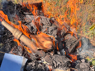 Fire consumes paper and wood in an outdoor setting during daylight hours