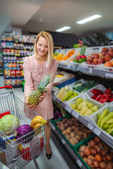 Woman buying fresh pineapple choosing healthy groceries in supermarket