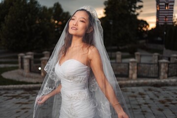 Asian bride wearing wedding dress and veil at sunset