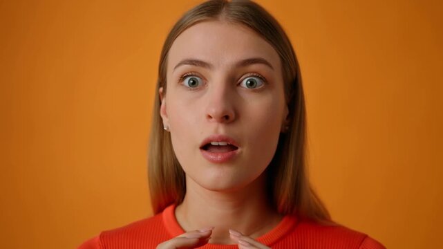 A portrait of a surprised young woman with open mouth and wide eyes against an orange background. Her expression is one of shock and disbelief Stock Video