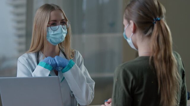 Caucasian woman doctor consulting girl patient in clinic hospital nurse gynecologist therapist practitioner in uniform medical mask talking with visitor medicine health advice consult communicate