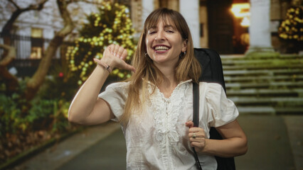 Fototapeta premium Woman points thumb to chest while carrying a guitar case on a city street near building steps; confidence celebration.