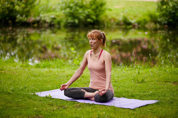 Woman, yoga and lotus for meditation at park, breathing exercise and wellness on lawn by river. Person, mindfulness and holistic fitness in summer with self care, chakra and zen by stream in nature