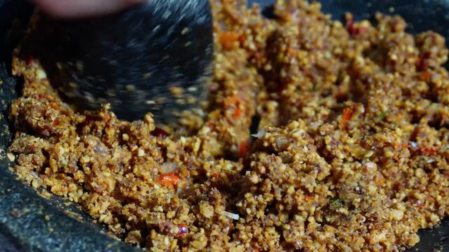 Hand grinding peanut chili paste using traditional stone mortar