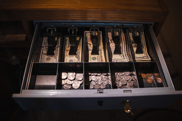 Open cash register drawer filled with organized US banknotes and assorted coins in compartments.