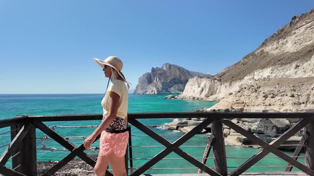 Woman feeling free and happy on wooden viewing platform of Mughsayl Beach in Oman close to Salalah.Enjoying the sunny weather and breathtaking coastal scenery with turquoise water and cliffs in Dhofar