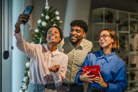 Diverse friends taking selfie celebrating office christmas party with gift - Powered by Adobe