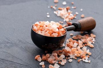 Himalayan pink salt crystals on a measuring spoon on a grey stone background.