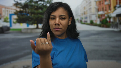 Woman in blue shirt points finger directly at camera on a busy city street with blurred buildings...
