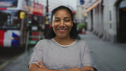 Woman in white striped shirt stands with arms crossed on a bustling city street lined with blurred...