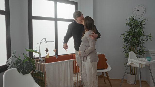 Pregnant woman and man in cozy room with crib sharing an intimate moment as they prepare for baby arrival, surrounded by soft lighting and home decor enhancing their anticipation. - Powered by Adobe
