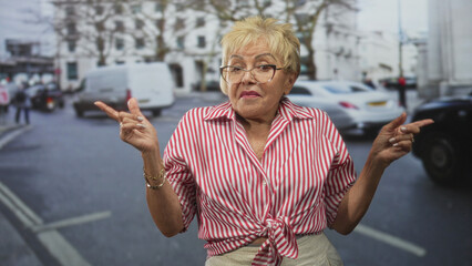 Woman pointing fingers and flashing a peace sign with visible hands and glasses in striped tied shirt on an urban street; cheerful confidence.