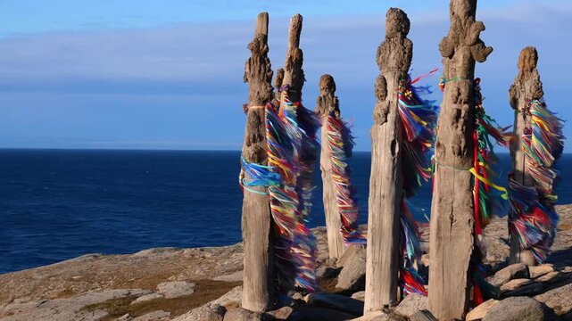 Ancient totems on a cliff overlooking the vast ocean with colorful prayer flags fluttering in the breeze. The structures stand tall against the backdrop of the sea and sky. Stock Video