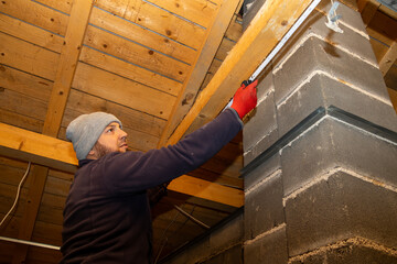 Worker checks alignment or fastening at the top of a brick column in the attic using a tool, demonstrating structural inspection and adjustment during a home renovation.