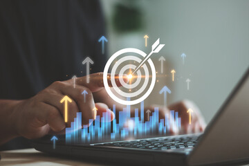 Person pointing digital target icon with virtual rising arrows and bar chart on laptop, symbolizing...