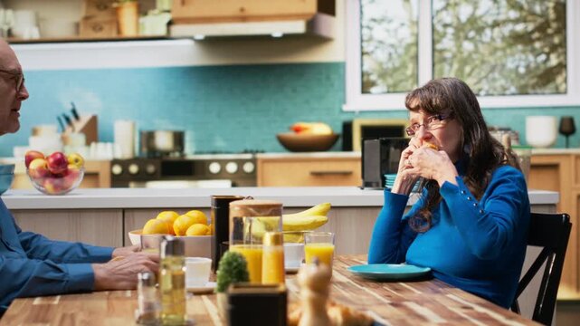 Mature wife feeling bothered and indifferent as elderly man continues chatting. Exasperated mood highlighting moment of monotony and relationship strain in retirement at home. Camera B.