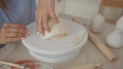 Woman hands smoothing white clay over a rotating wheel platform in a sunlit studio workspace; serenity.