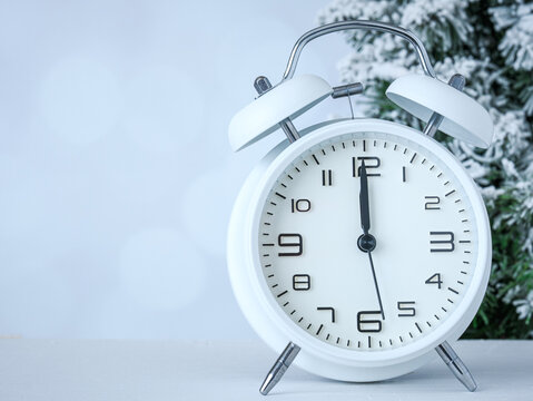 New Year’s midnight clock with winter snow on spruce pine tree on a blurry gray backdrop. Celebration for the new year. 