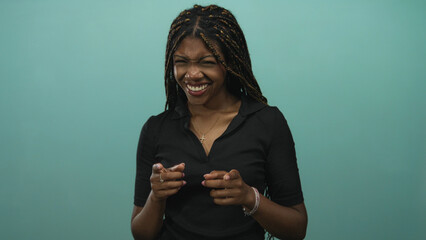 Woman pointing finger and smiling in teal studio, braided hair and hands gesturing toward camera;...