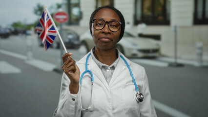 Woman wearing a white coat holding a british flag on an urban street with blurred buildings, stethoscope visible, expressing diversity in a multicultural city setting.