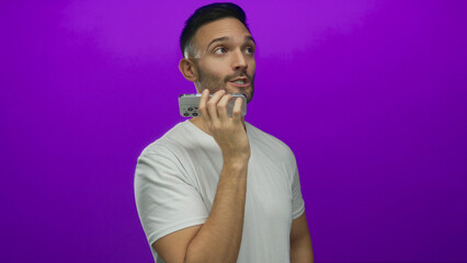Young hispanic man talking on smartphone against vibrant purple background wearing casual white shirt.