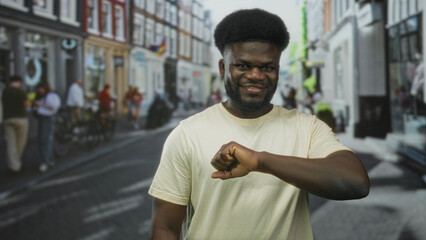 Man pointing fist at camera on busy city street smiling broadly and leaning forward, wearing pale...