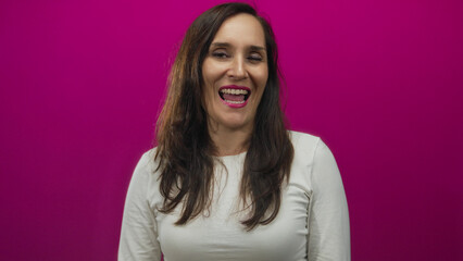 Fototapeta premium Young hispanic woman smiling against a vibrant pink background, exuding confidence and joy in a studio setting with a cheerful and positive demeanor.
