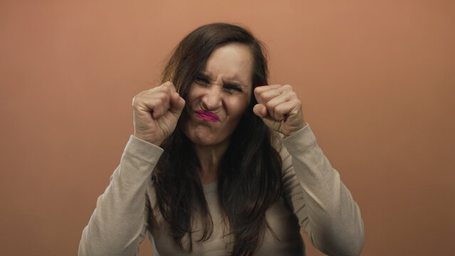 Young hispanic woman clenches fists by face scrunching facial features making crying gesture in studio; sadness grief.