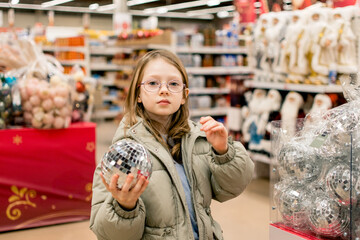 Fototapeta premium A girl in a store among Christmas decorations. Preparing for the New Year and Christmas. Buying decorations and gifts.