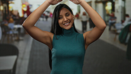 Young woman making a playful gesture on an outdoor restaurant terrace, surrounded by people and a...