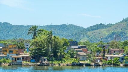 Vibrant waterfront community with modest houses and lush tropical vegetation, set against a backdrop of green, hilly mountains