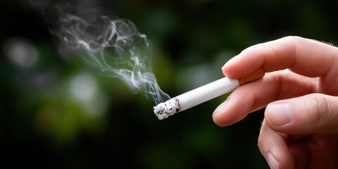 Hand Holding Cigarette with Smoke Against a Blurred Natural Background in Soft Lighting
