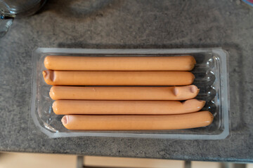 A pack of five sausages neatly arranged within a transparent tray, resting on a dark textured surface. Ideal for food advertisements, recipes, and culinary presentations.