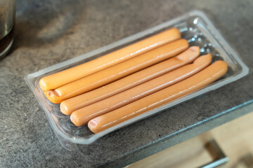 Pack of sausages displayed in a clear plastic container on a kitchen countertop, showcasing their smooth texture and light pink color, ideal for meal preparation or cooking.