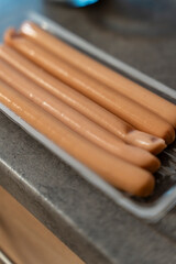 A close-up of several sausages placed in a clear plastic tray on a dark countertop. These sausages are ready for cooking or serving at a meal, showcasing their smooth texture.