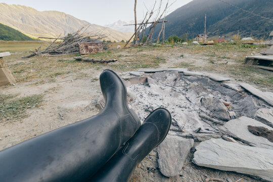boots by a cold campfire with grey ashes, relaxed view of distant mountains and open countryside, outdoors camping scene with rustic seating and minimal gear for a quiet nature break