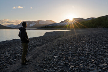 Hiker watching sunset over Gjevilvatnet lake and mountains, Norway