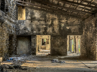 Interior of an abandoned, burned house with charred stone walls, soot marks, and debris on the floor. Light enters by doorways, revealing structural damage highlighting fire risk and cleanup needs.